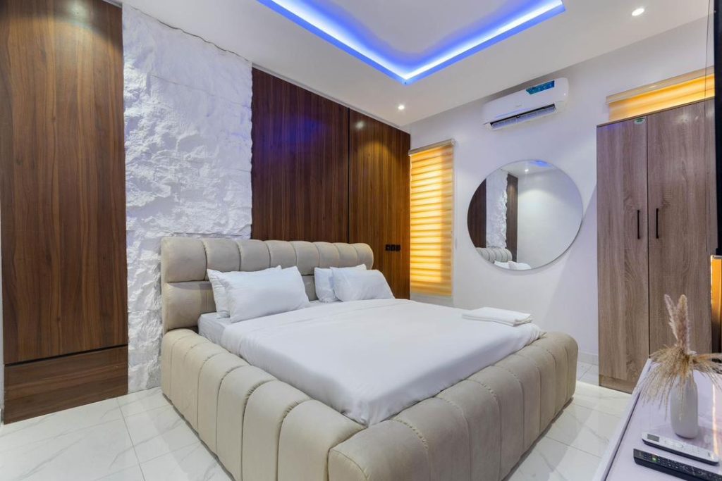 Made-up bedroom in a furnished Nigerian short-let apartment with walnut wardrobes and blue cove lighting