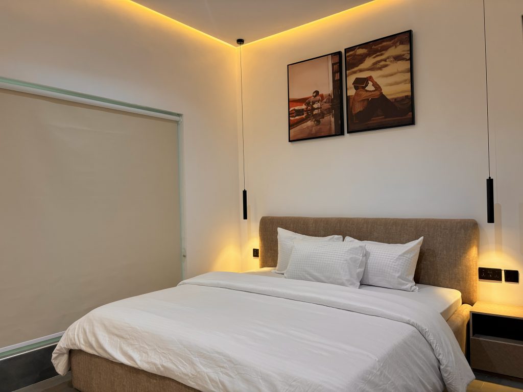 A made hotel-style bed with white linen, framed prints above and bedside lighting